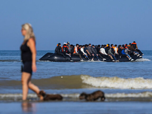 TOPSHOT - A tourist walks her dogs as migrants board a smuggler's boat in an attempt